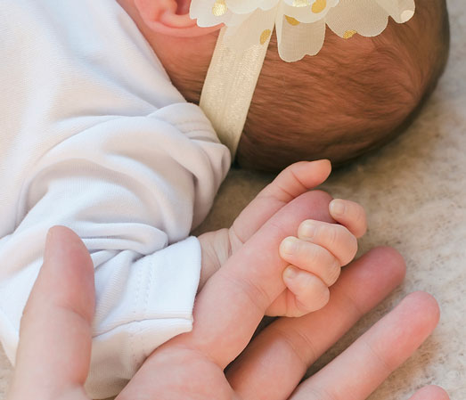 Newborn baby holding parent's finger after delivery